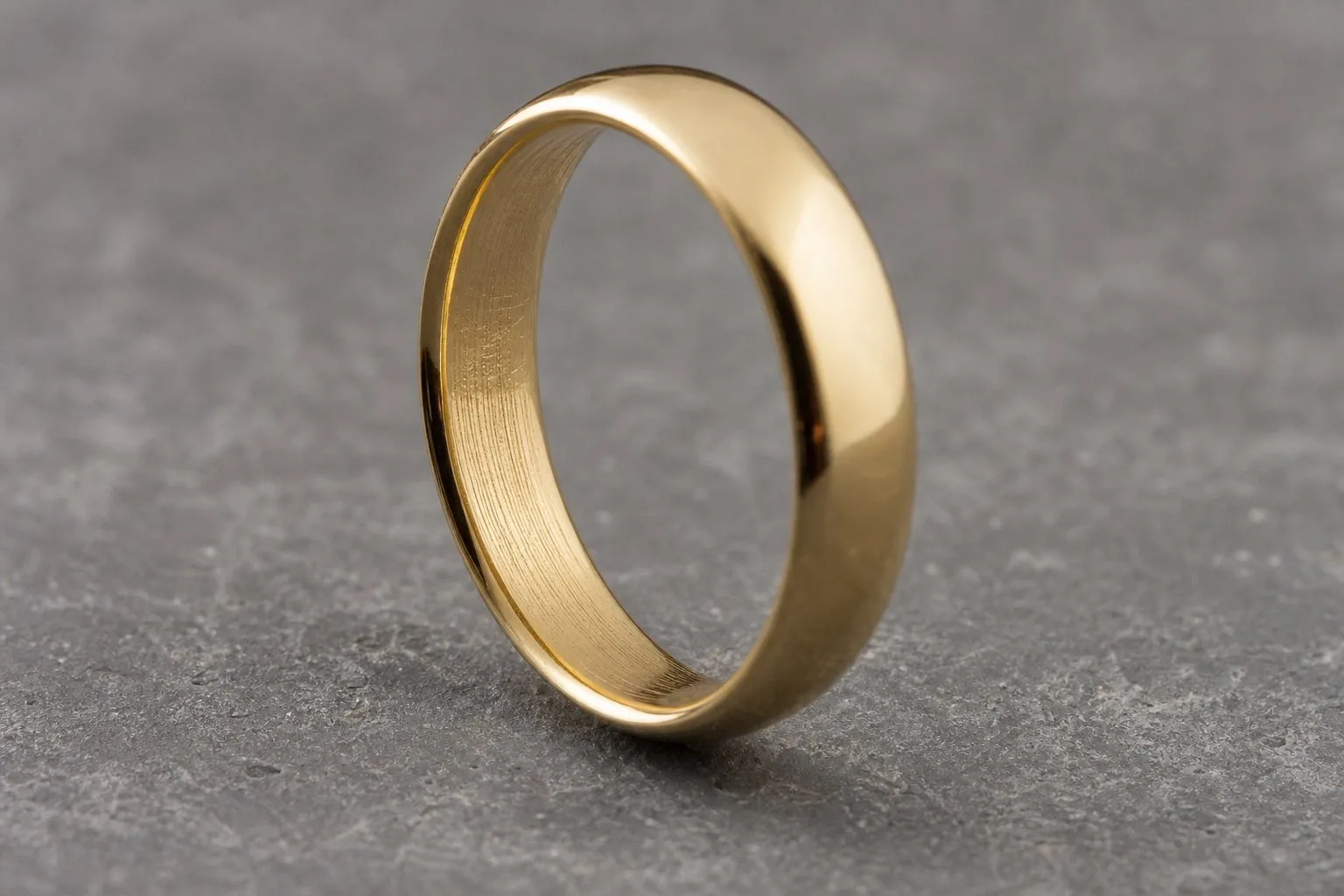 A plain gold wedding ring standing upright showing faint abstract tooling marks inside the hoop