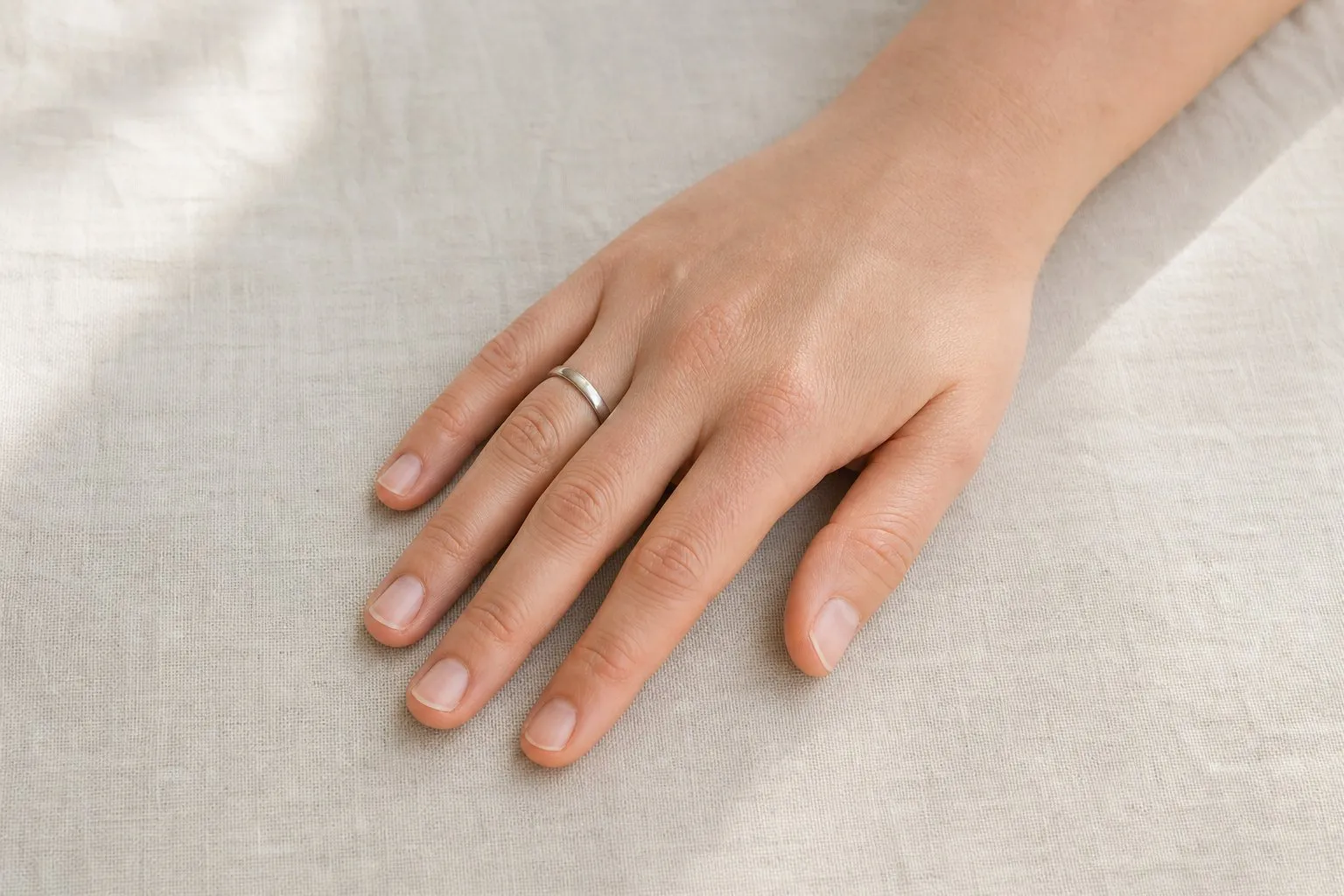 One hand resting palm down and relaxed on a pale linen cloth