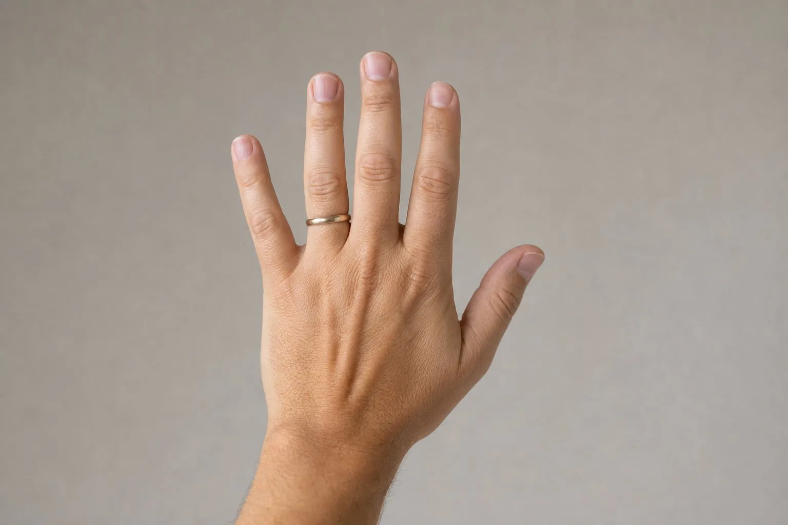 One hand held loosely half open at chest height against a plain putty gray background