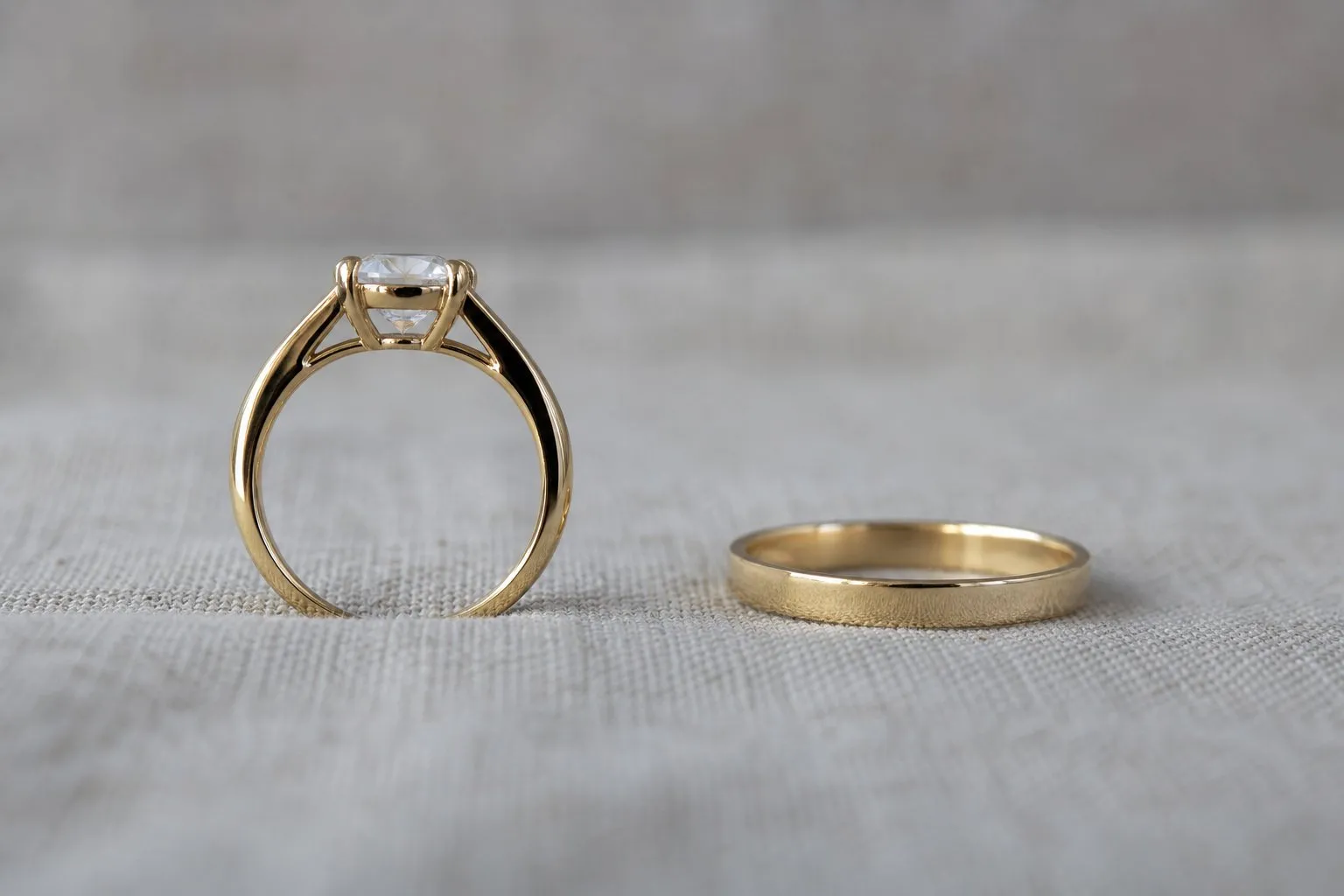 A cathedral setting seen from the side beside a plain flat wedding band on gray linen