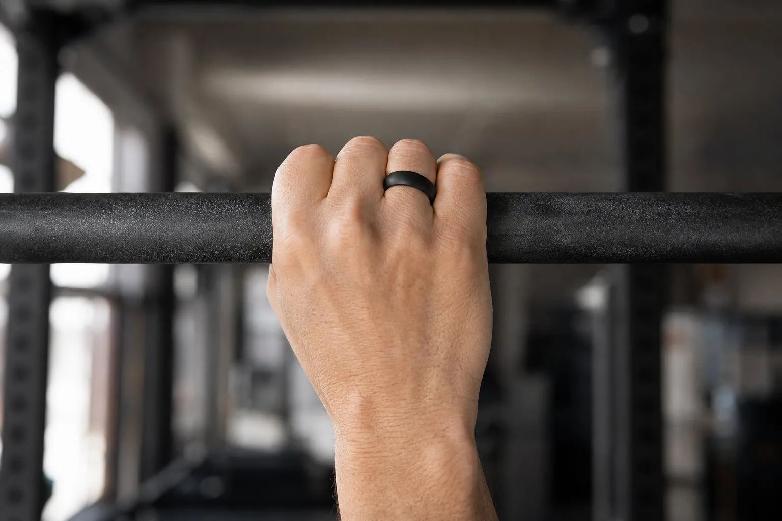 A hand gripping a pull-up bar wearing a black silicone wedding ring for working out