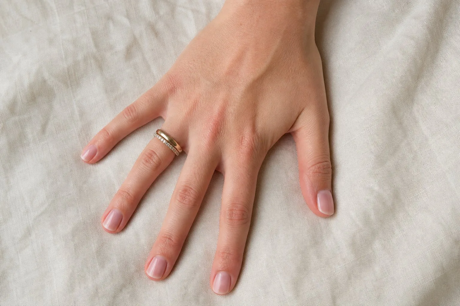 A plain band stacked with an eternity band on a hand resting on linen