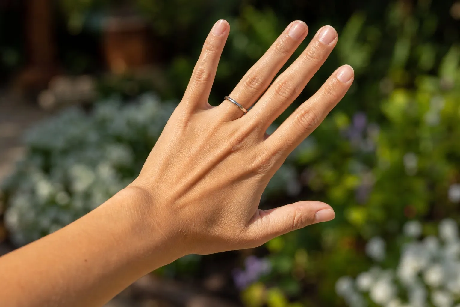 An open hand wearing only a plain narrow band on the ring finger, outdoors in late afternoon light