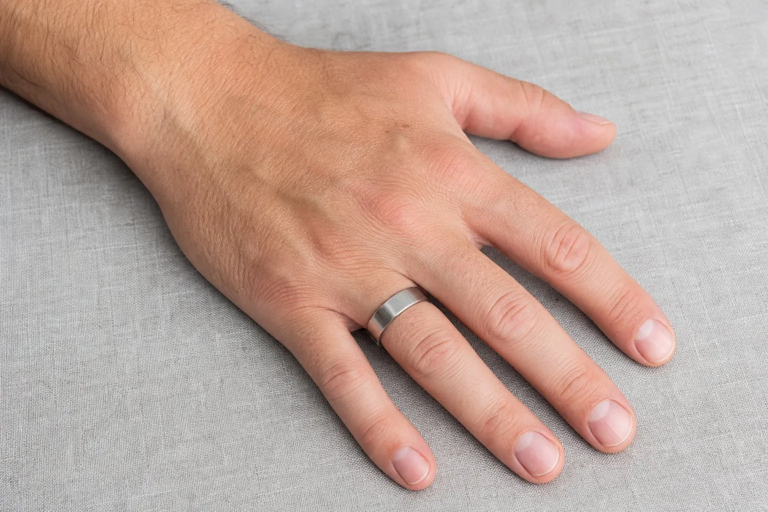 One man's hand resting palm down wearing a single plain wide metal band